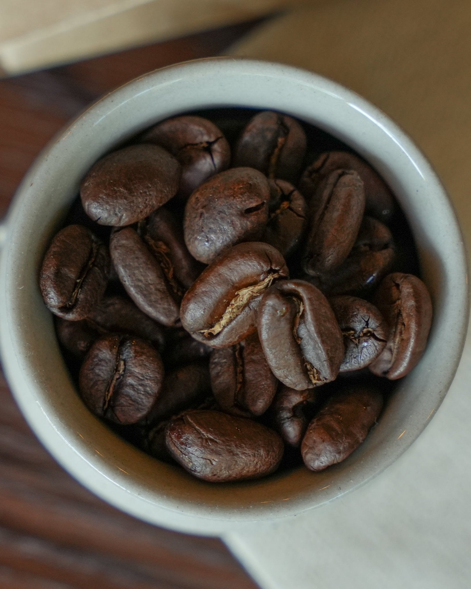 Close-up of freshly roasted Brazilian Santos coffee beans in a white ceramic cup, showcasing their rich brown color and distinct texture, perfect for highlighting the medium roast of this premium Shopify product.