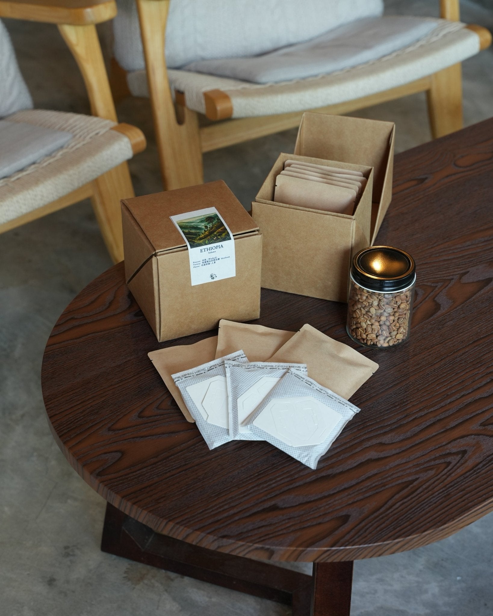 Coffee brewing set with eco-friendly packaging on wooden table, including boxes, filter bags, and jar of coffee beans, in a minimalist cafe setting