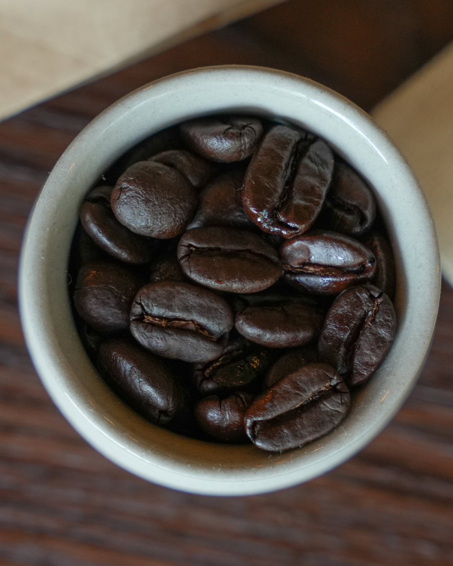 Dark roasted Sumatran coffee beans in a white ceramic cup, showcasing the rich, oily texture of Typica beans from Indonesia, ideal for Sip Coffee&