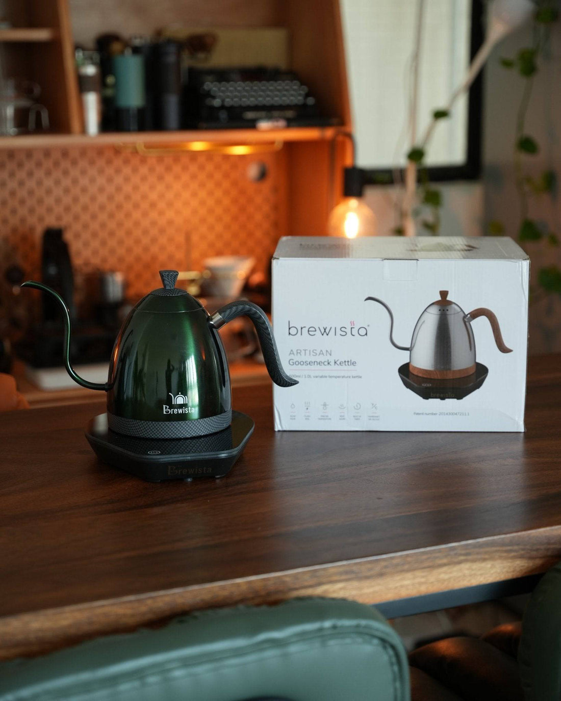 Brewista Artisan temperature-controlled kettle displayed on wooden countertop with product box, showcasing sleek green design and gooseneck spout in cozy kitchen setting