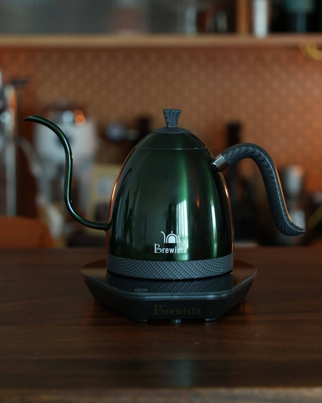Brewista Artisan temperature-controlled kettle with gooseneck spout on wooden countertop, featuring sleek dark green design and digital base for precise brewing