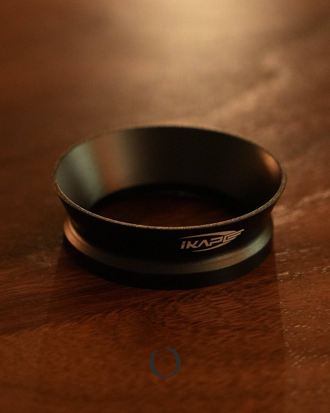 IKAPE V2 magnetic dosing ring for espresso machines, black aluminum alloy, on wooden surface in warm lighting, enhancing barista workflow efficiency