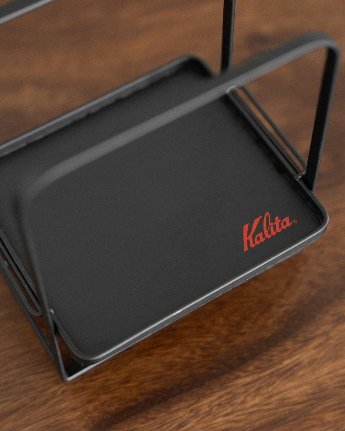 Kalita adjustable coffee dripper stand with black metal frame and tray, featuring red Kalita logo, on wooden surface. Sturdy design for stable coffee brewing.
