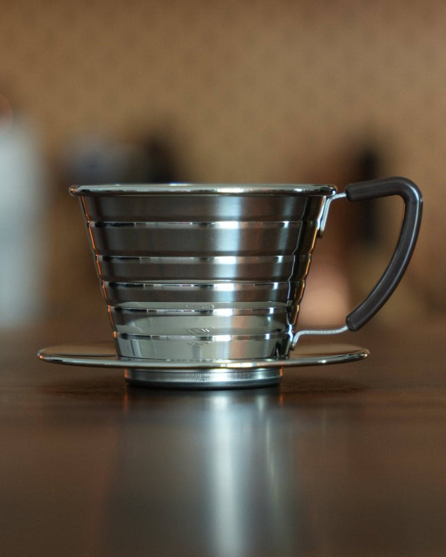 Kalita Wave 155 S stainless steel pour-over coffee dripper with distinctive wave pattern design, showcasing its durable construction and elegant form on a wooden surface