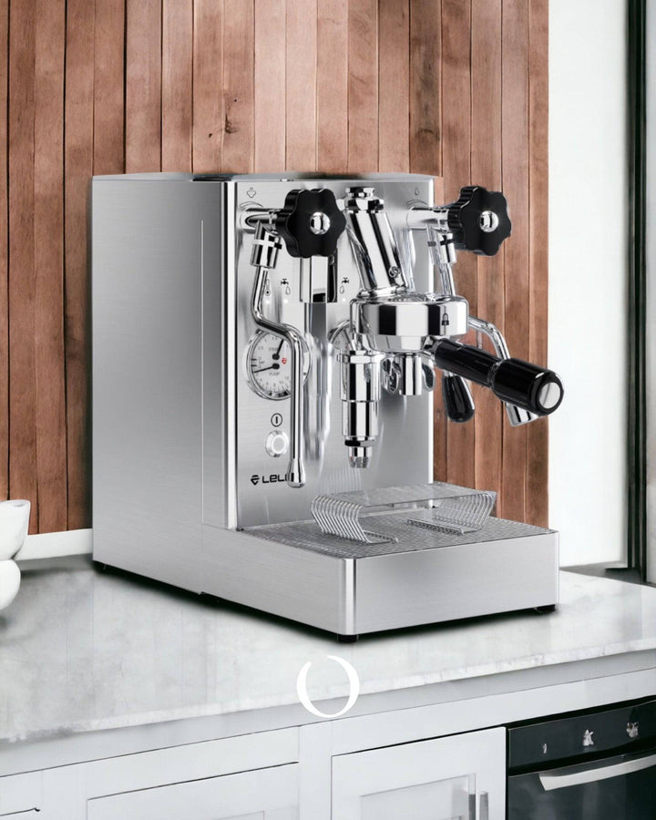 Lelit MaraX V2 PL62X espresso machine with stainless steel body, dual pressure gauges, and wooden knobs on marble countertop against rustic wooden wall background