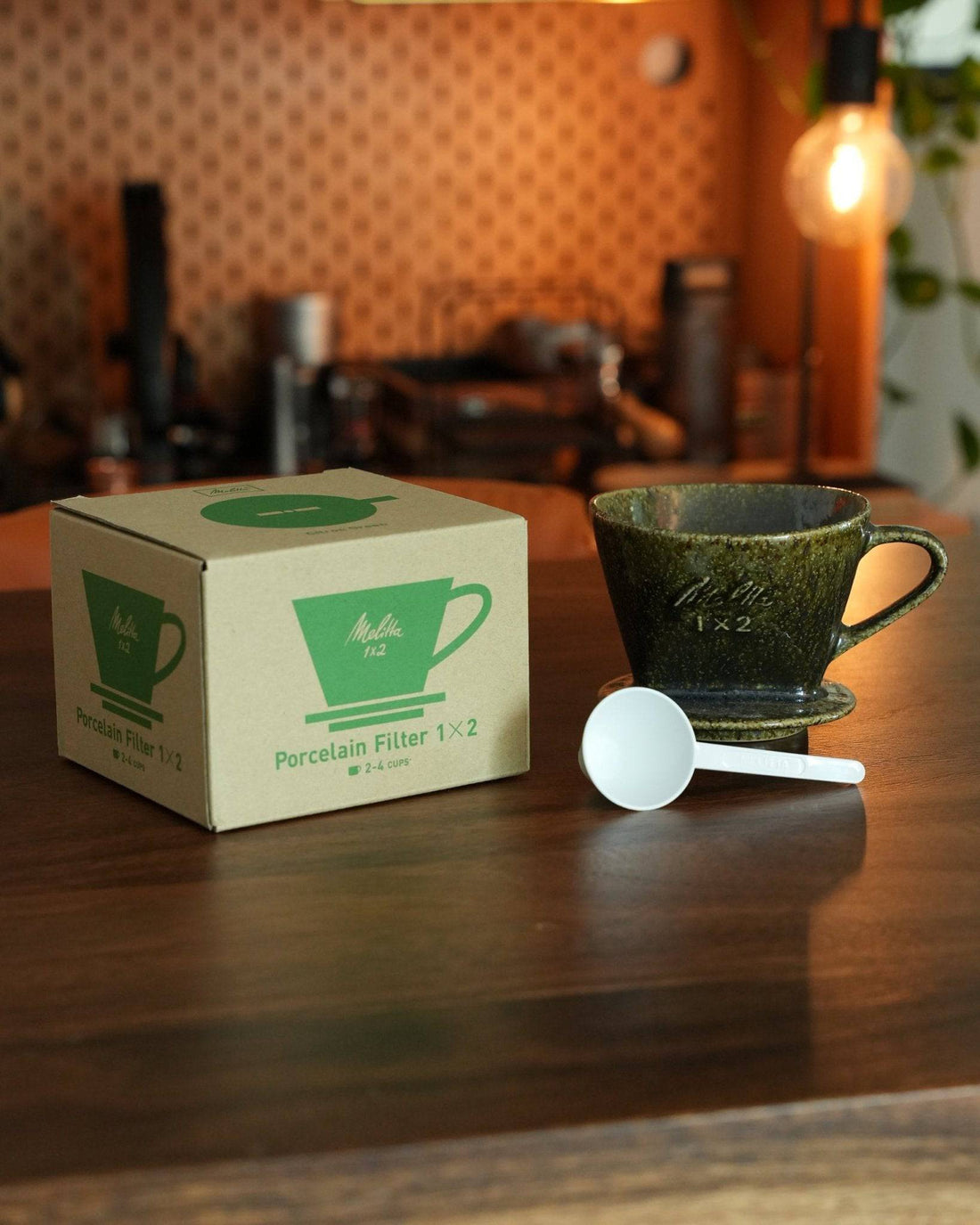 Melitta yellow-green ceramic pour-over coffee dripper with box and measuring spoon on wooden table, coffee equipment in background