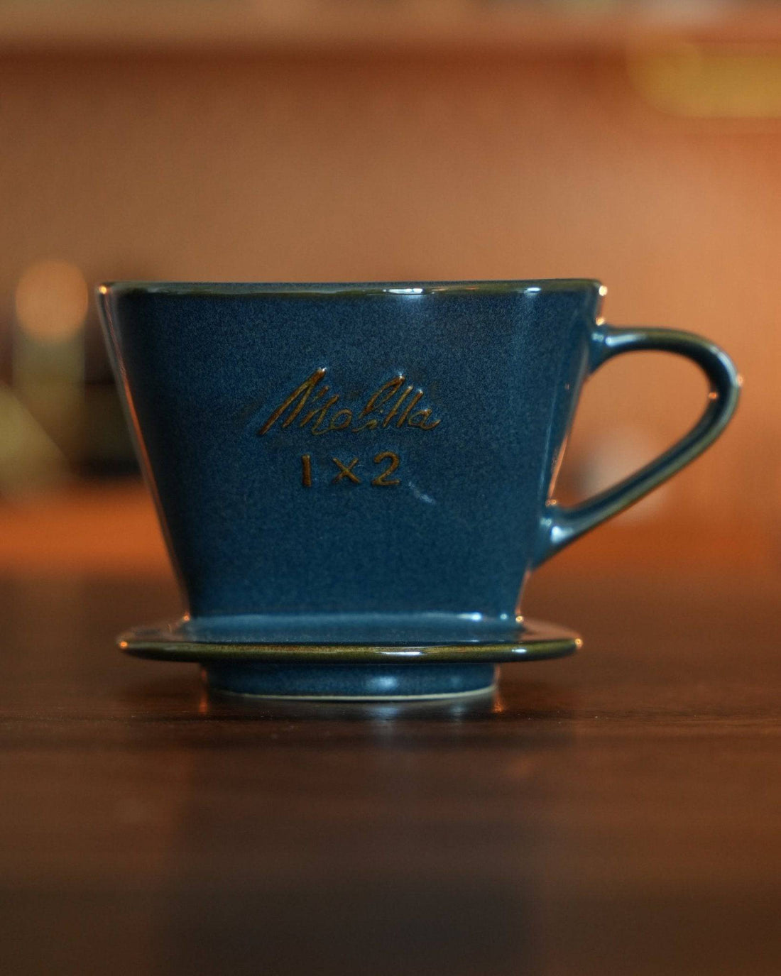Melitta turquoise blue pour-over coffee dripper with gold lettering, placed on wooden surface, showcasing elegant design and premium craftsmanship of Japanese Mino-yaki pottery