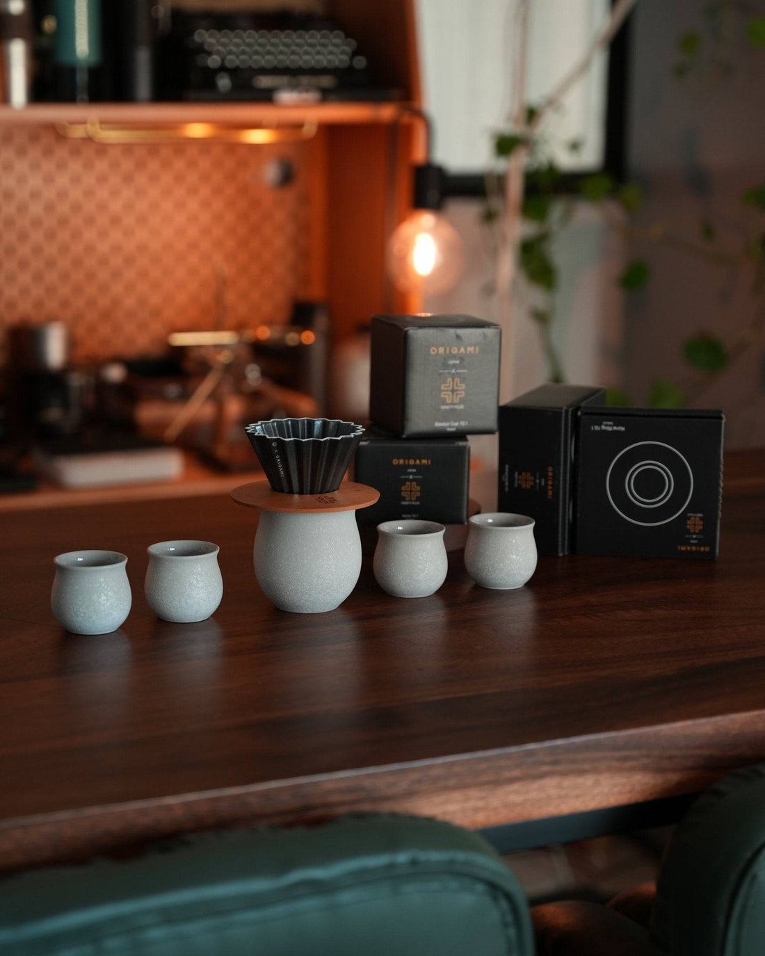 Ninety Plus pour-over coffee brewing set featuring white ceramic cups, a dripper, and premium coffee packages on a wooden table, set against a warm, cozy cafe background with soft lighting