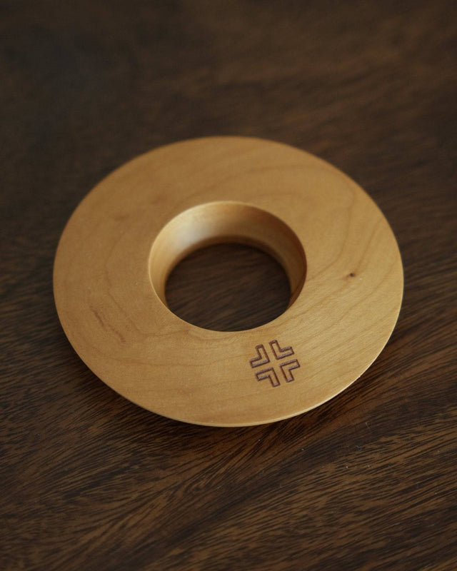 Ninety Plus Coffee Kone Ring 10.1 in cherry wood color, circular wooden base for mini pour-over coffee dripper, featuring a central hole and engraved logo, displayed on dark wood surface