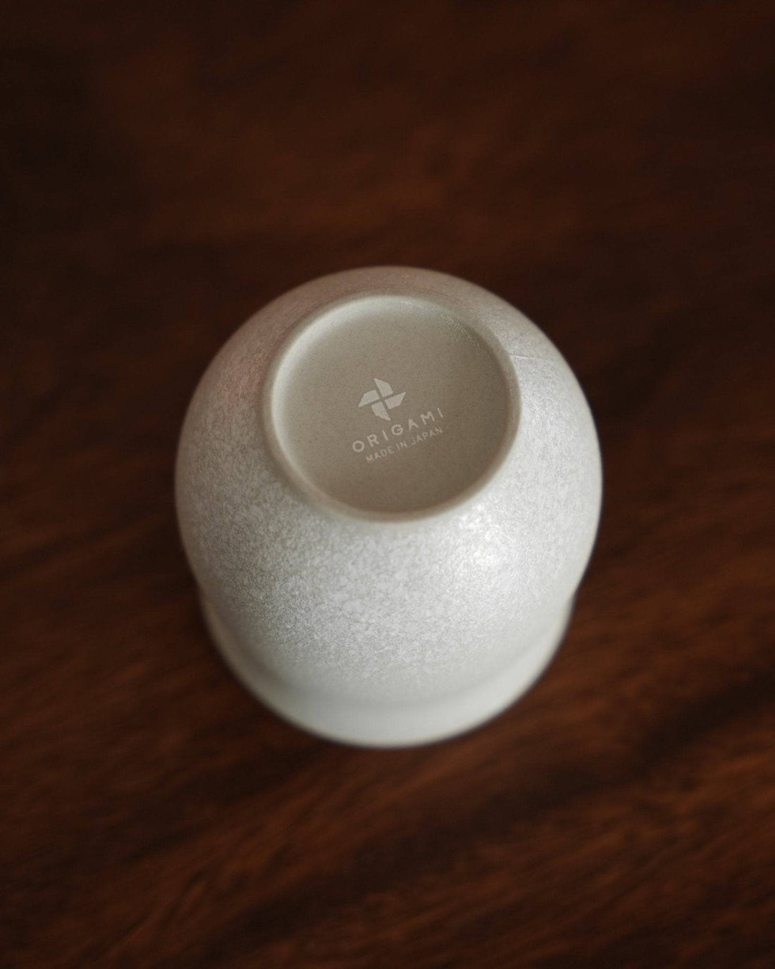 Ninety Plus Coffee Savour Cup 10.1 in Basalt white, designed by Origami, showcasing its unique shape and texture on a dark wooden surface. The cup&