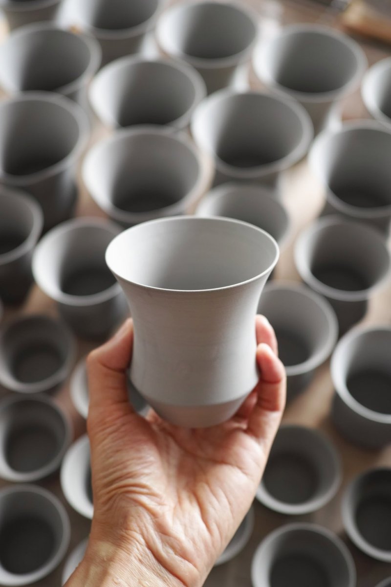 An unglazed cup body held by hand in the workshop