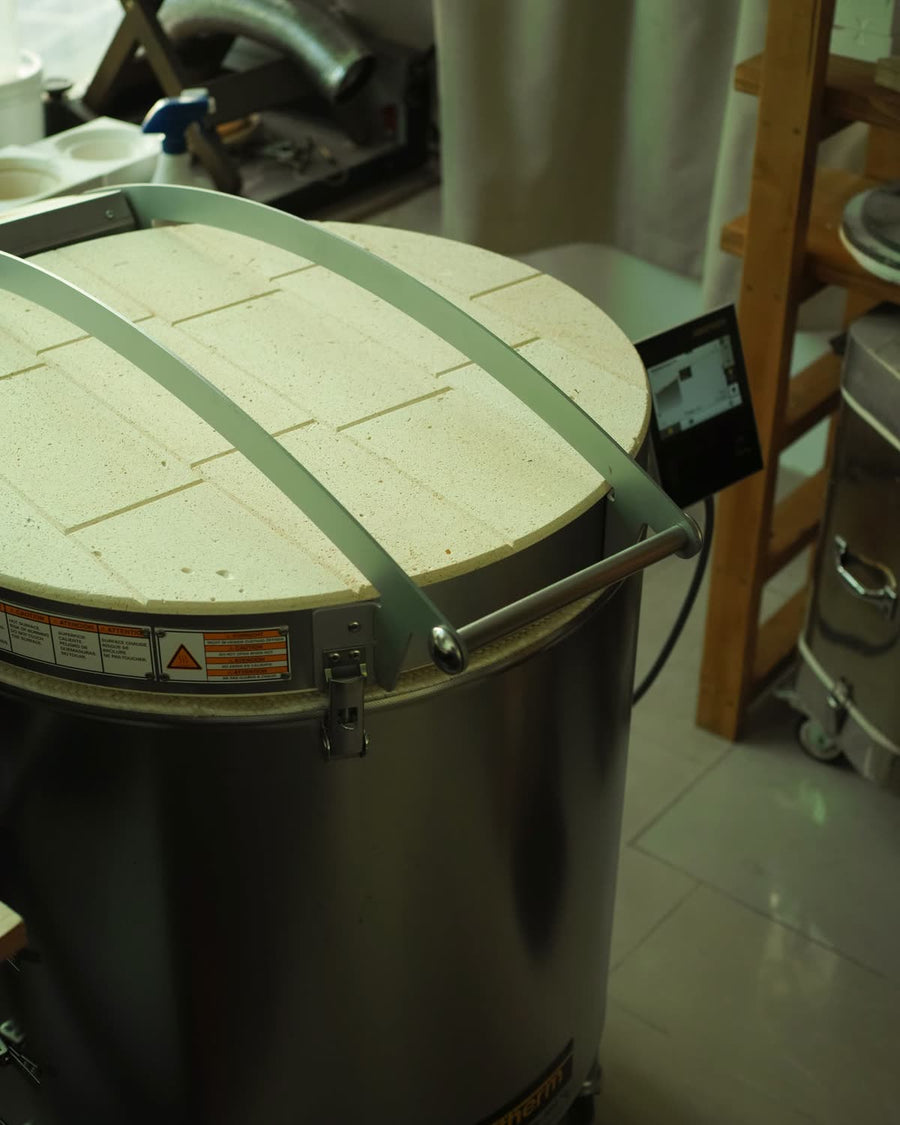 The lid of a large electric kiln is closed and latched, with the temperature-control panel beside it