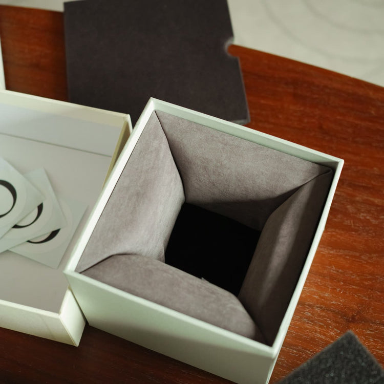 Inside the gift box, a folded grey insert forms a square recess for the cup