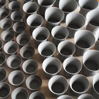 A row of unglazed cup bodies drying slowly with their openings facing upwards on a wooden board, photographed from above