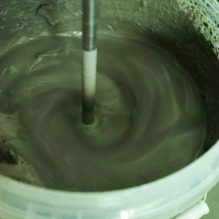 A mixing stick stirring slip in a white plastic bucket, creating a whirlpool on the surface