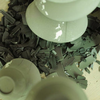 An unglazed cup body placed upside down on a wooden table beside dark clay shavings removed during trimming