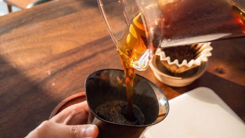 Alpha in Ember Black Gold held while pour-over coffee is poured from a coffee server into the recessed opening
