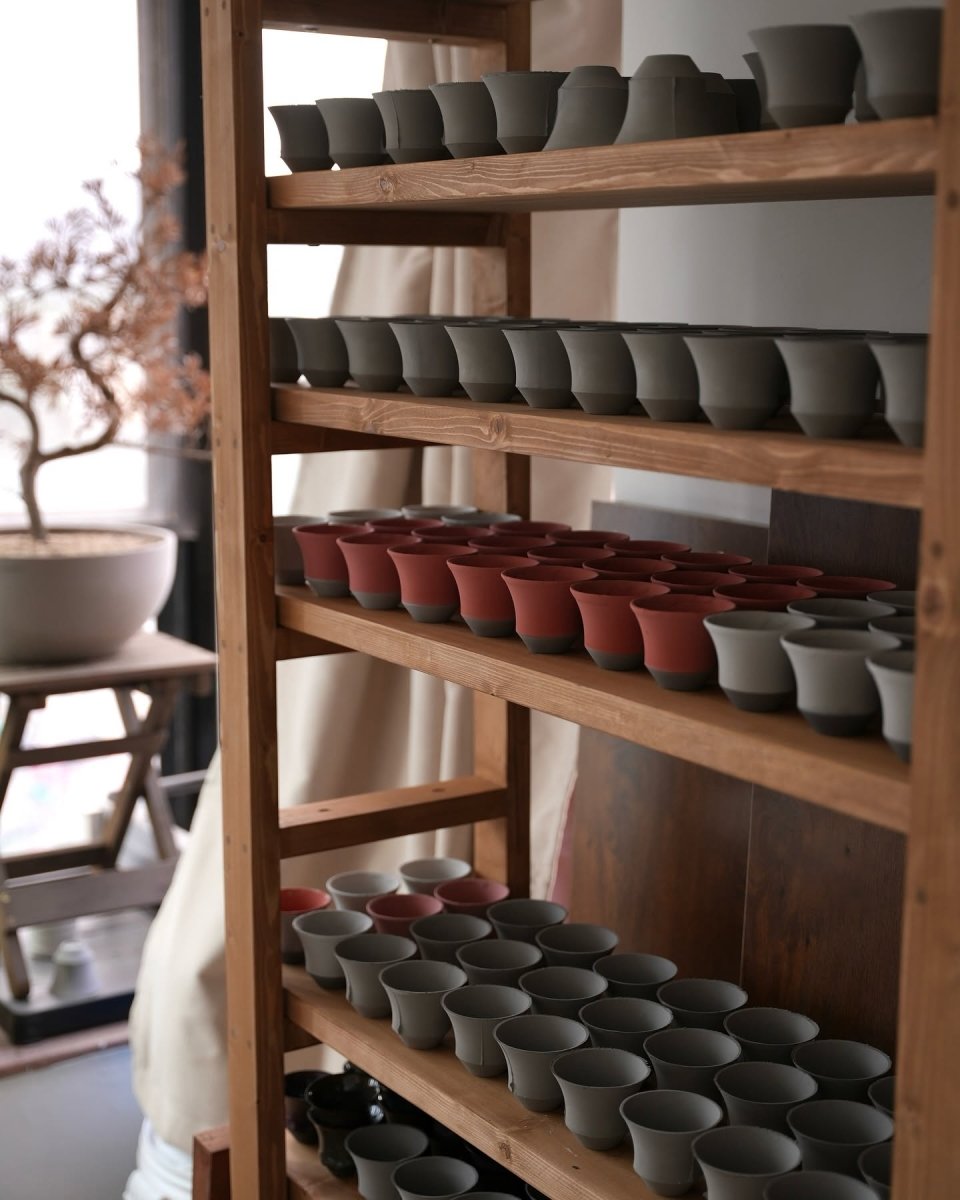 A five-shelf pine rack in the workshop, filled with cups in different clays and colours
